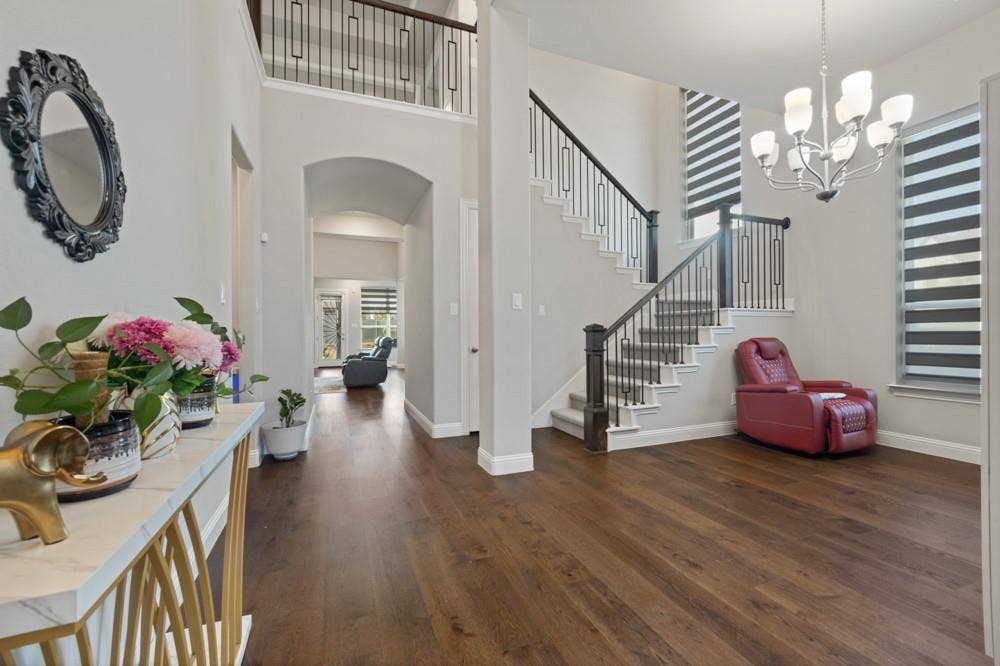 Wood-finish flooring throughout, an open-tread staircase with wrought iron balusters, a decorative light fixture, and arched doorways