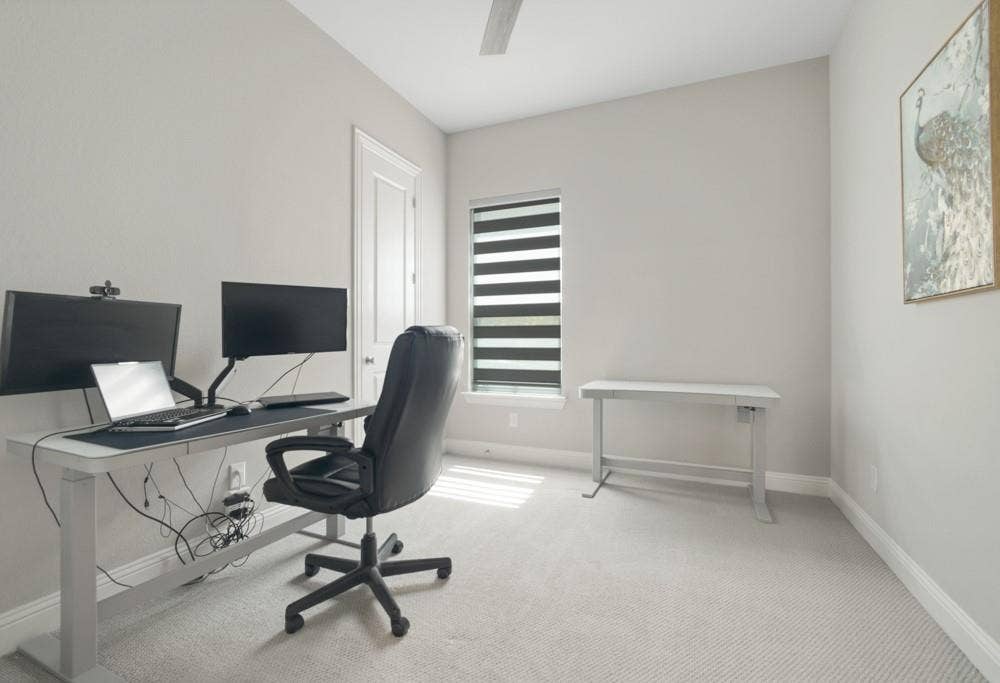 Neutral wall finishes, textured carpeting, a single window with horizontal blinds, and a ceiling fan
