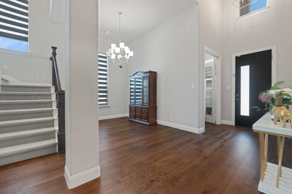 Wood-finish flooring, staircase with carpeted treads, contemporary chandelier, and a front entry door with a vertical frosted glass panel