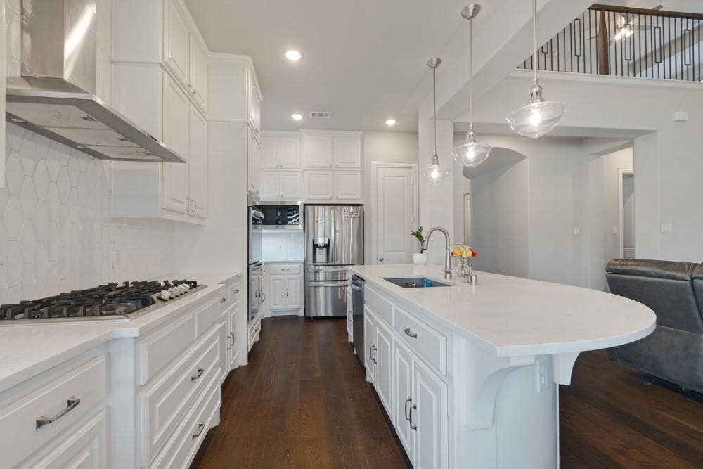Kitchen featuring white cabinetry, a central island with an undermount sink, stainless steel appliances, and wood-finish flooring