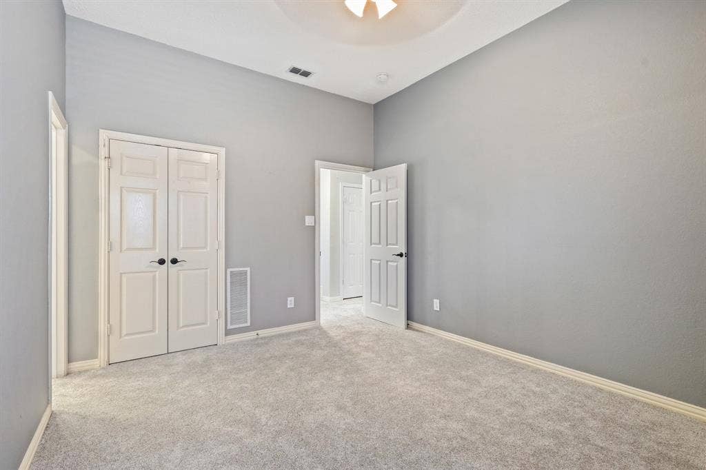 High-ceilinged room featuring neutral wall tones, plush wall-to-wall carpeting, and double-door closet cabinetry with matte black hardware