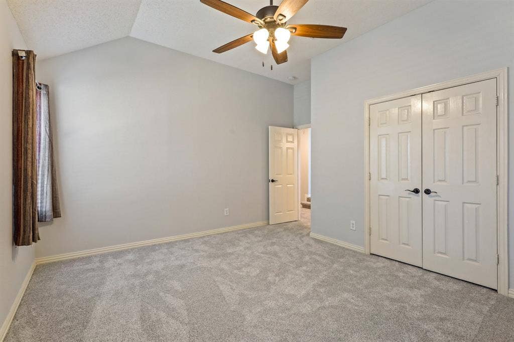 Vaulted ceiling with a centrally mounted ceiling fan, neutral carpeting, and dual-panel closet doors