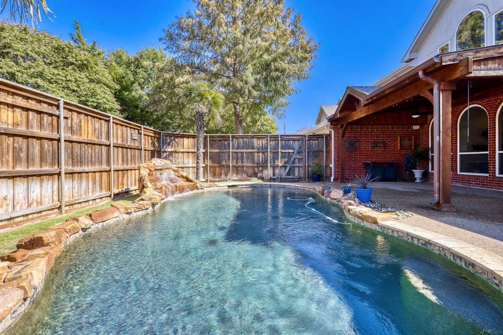 Backyard pool featuring a rock-lined water feature, stone coping, and a covered patio with a wooden beam structure and red brick exterior