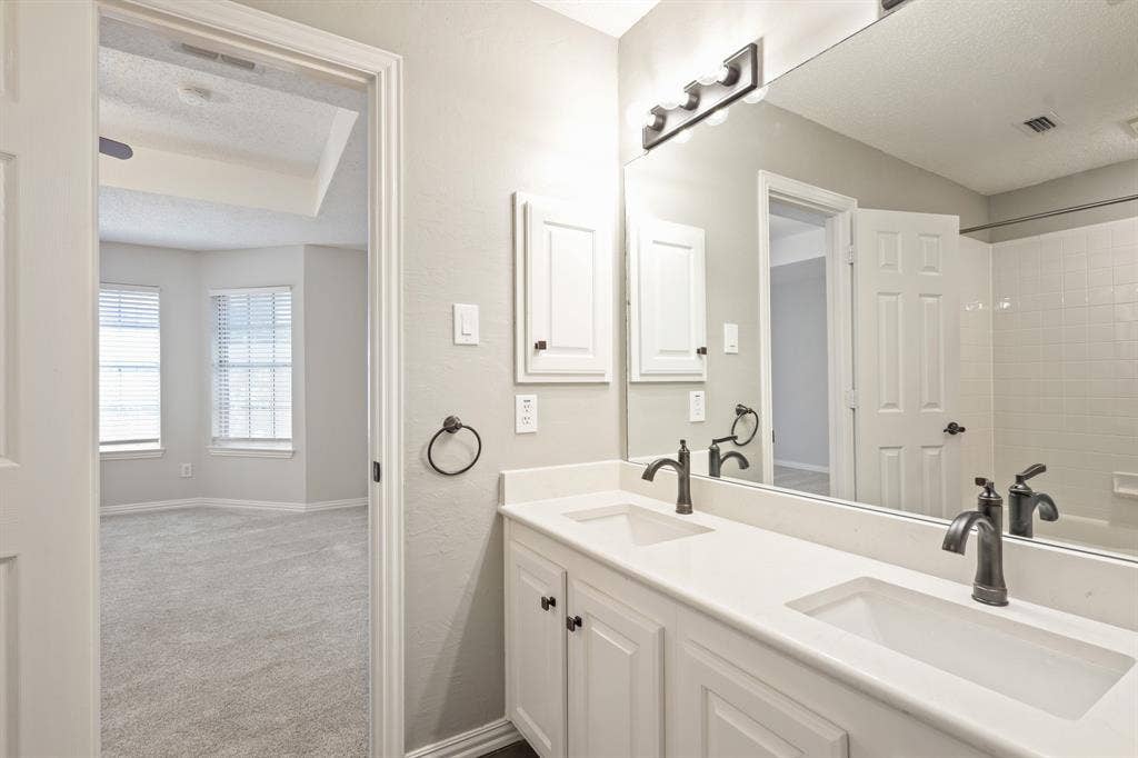 Dual-sink vanity with white cabinetry, solid surface countertop, oil-rubbed bronze faucets, and full-width vanity mirror
