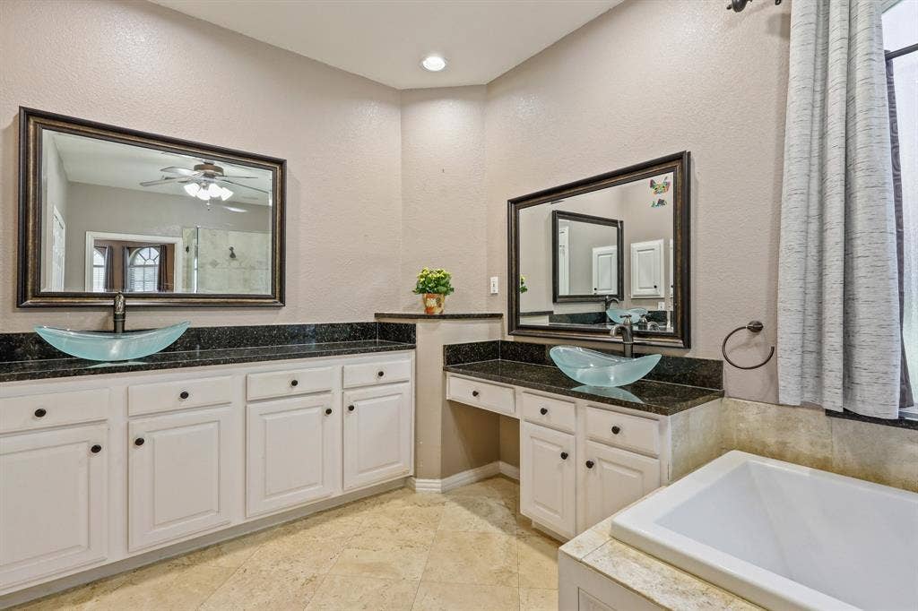 Dual vanity featuring white cabinetry, dark stone countertops, glass vessel sinks, framed mirrors, and tile flooring