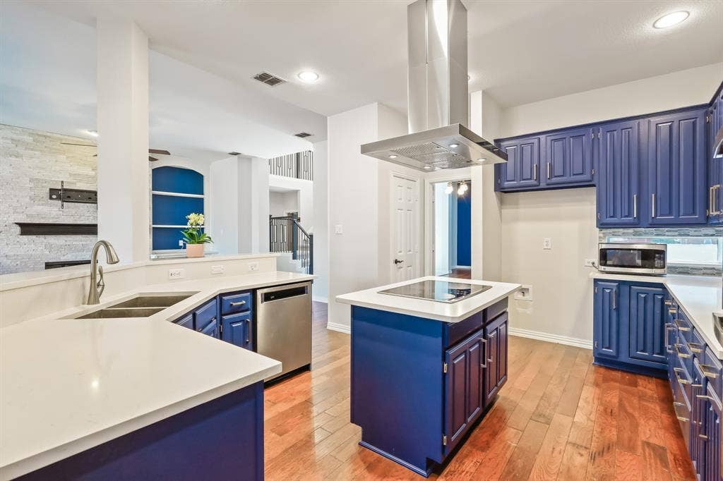 Kitchen featuring blue cabinetry, stone-finish countertops, stainless steel appliances, a center island with a built-in cooktop, and an overhead stainless steel ventilation hood