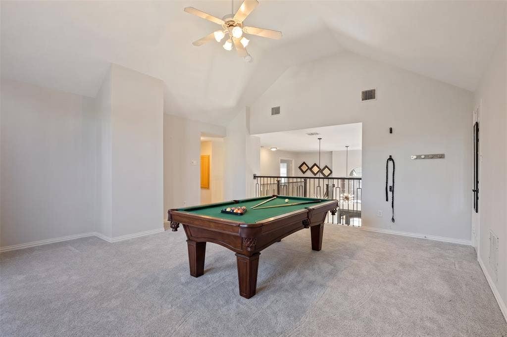 Vaulted ceiling featuring a central ceiling fan with multi-light fixture, carpeted flooring, and a metal balustrade railing