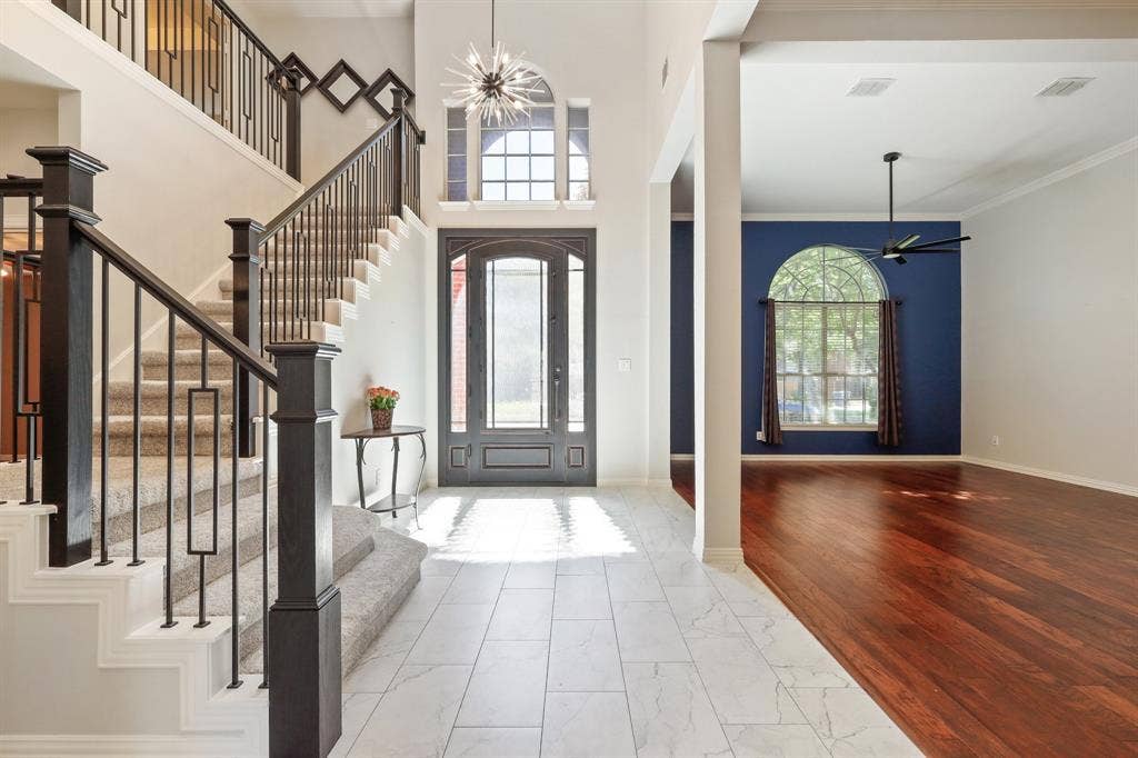 Grand foyer featuring stone-look tile flooring, an arched glass-paneled entry door, a starburst chandelier, and a staircase with decorative wrought iron railings