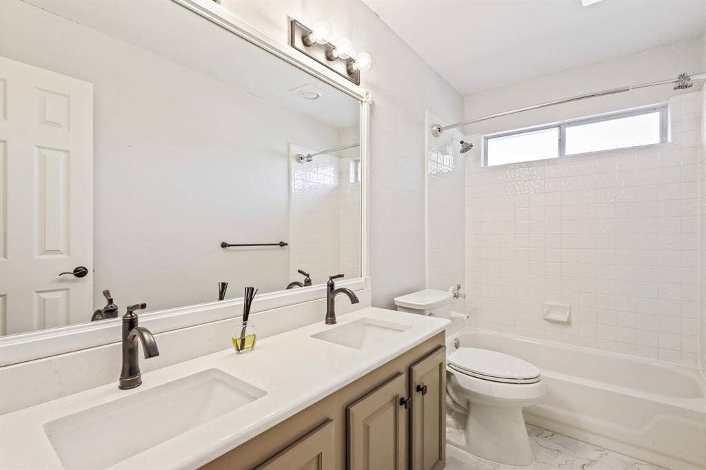Dual-sink vanity with quartz countertop, under-mount basins, dark finish fixtures, and full-width vanity mirror, complemented by a white tiled tub-shower combination