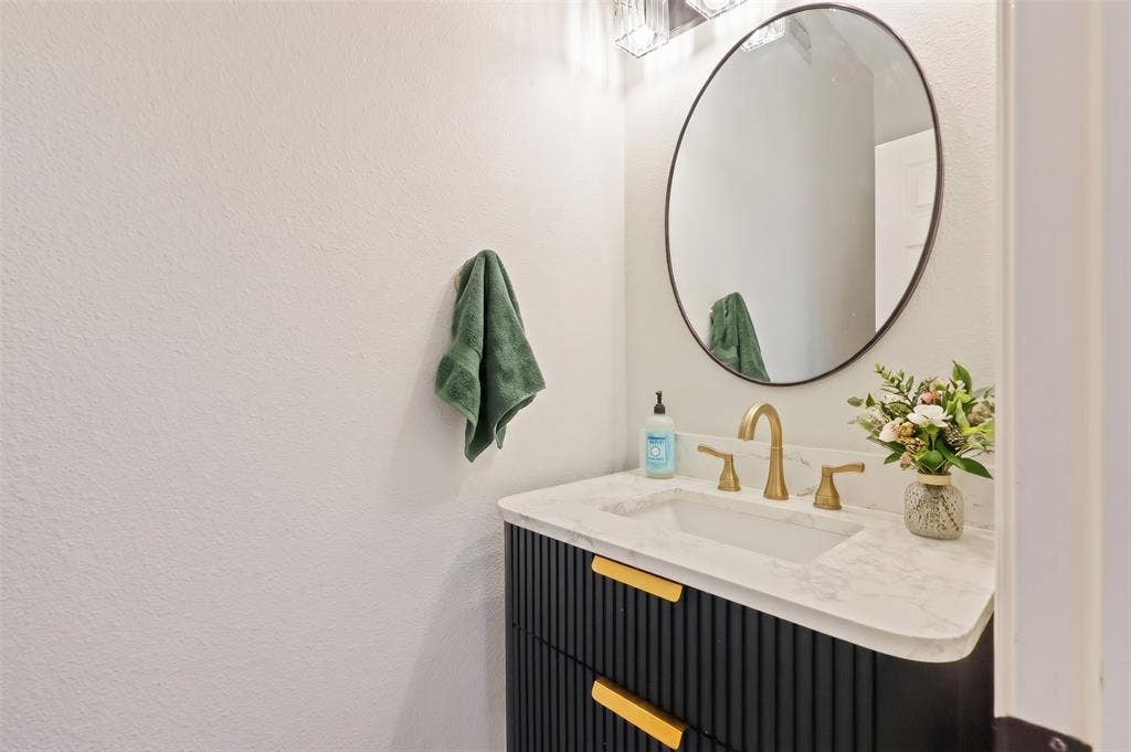 Dark-toned fluted vanity with gold hardware, stone-composite countertop, integrated rectangular sink, brass-finish widespread faucet, and oval mirror