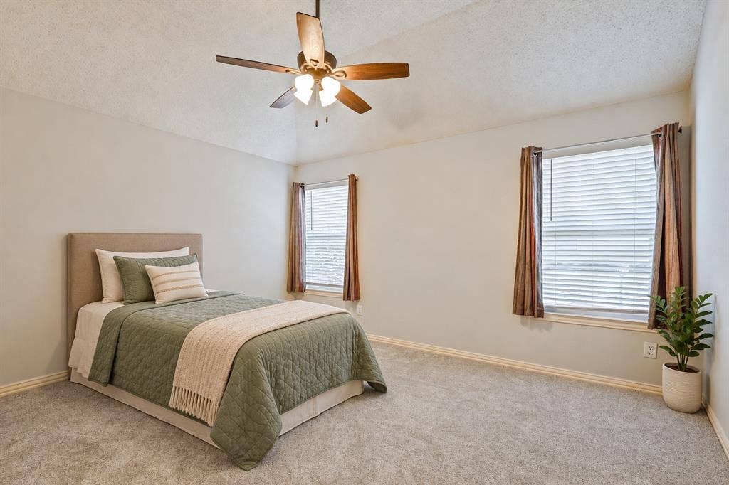 Vaulted ceiling with a central multi-blade ceiling fan, neutral wall tones, wall-to-wall carpeting, and dual windows ( virtually Staged)