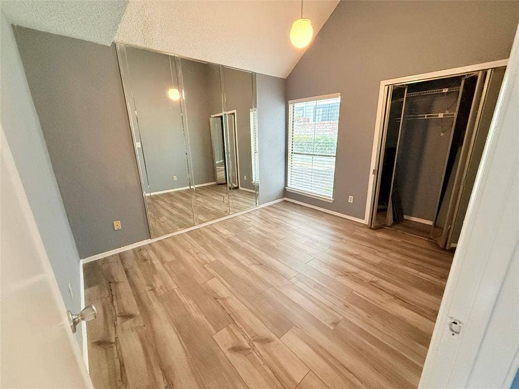 3402 Country Club Drive W, #154, Irving, TX 75038 Vaulted ceiling, wood-finish flooring, mirrored closet doors, window with blinds, and built-in closet organization