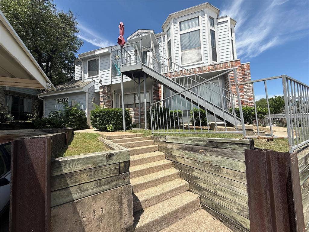 3402 Country Club Drive W, #154, Irving, TX 75038 Multi-level exterior featuring brick and siding, a private balcony with metal railings, an exterior staircase with metal railings, and concrete steps leading to the entrance