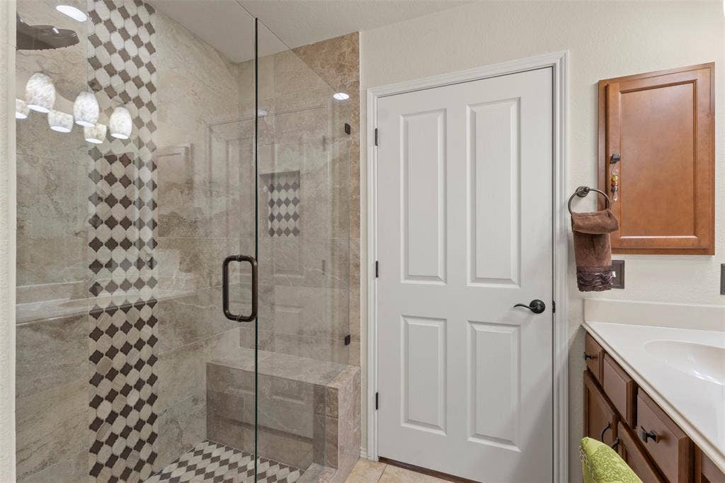146 Montague Lane, Frisco, TX 75036 Glass-enclosed shower with a patterned tile accent wall, built-in shower bench, and dark bronze hardware