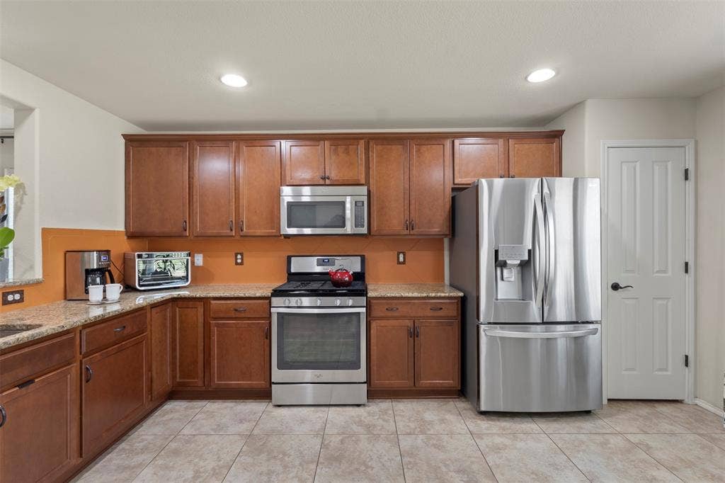146 Montague Lane, Frisco, TX 75036 Kitchen featuring wood cabinetry, stainless steel appliances, speckled countertops, and tile flooring