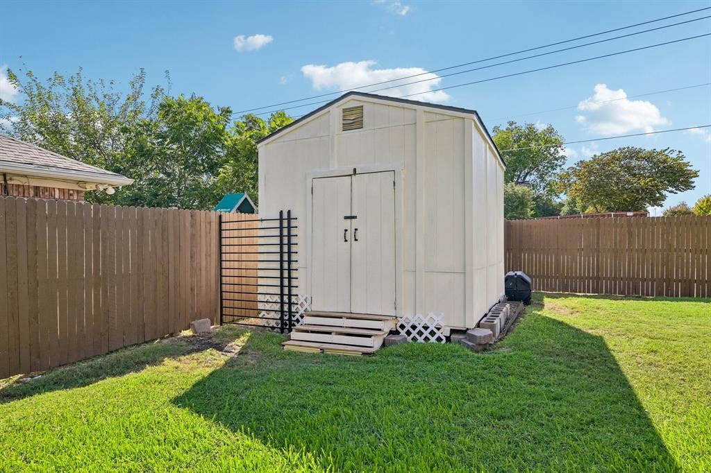 3441 Sheffield Circle, Plano, TX 75075 Backyard featuring a detached storage shed with double doors, wood fencing, and a grassy lawn