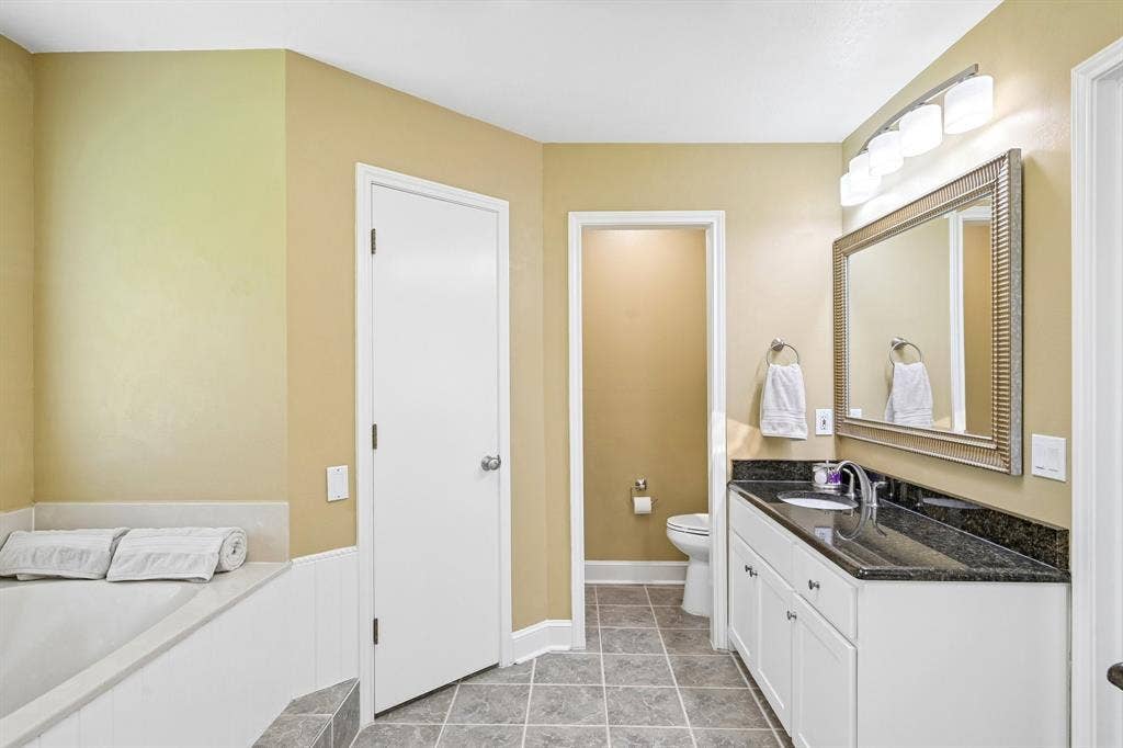 3441 Sheffield Circle, Plano, TX 75075 Spacious bathroom featuring a built-in bathtub, white vanity with ample storage, dark countertop, and a large framed mirror with overhead lighting