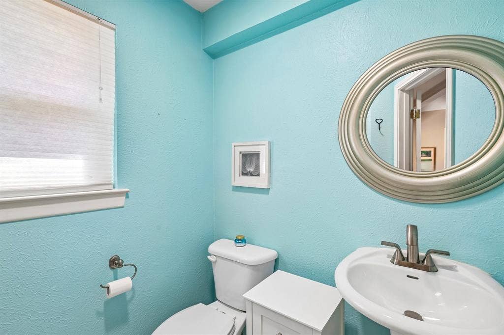 3441 Sheffield Circle, Plano, TX 75075 Pedestal sink with a brushed nickel faucet, coordinating oval mirror, and a window with pleated shades