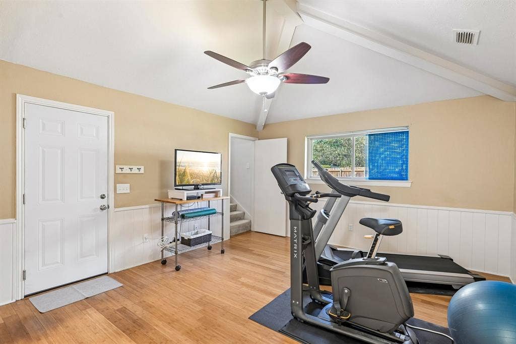 3441 Sheffield Circle, Plano, TX 75075 Vaulted ceiling with exposed beams, wood-finish flooring, half-wall wainscoting, and a ceiling fan