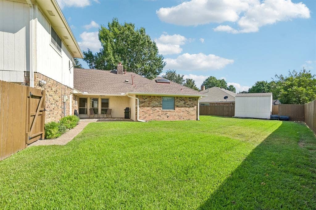 3441 Sheffield Circle, Plano, TX 75075 Expansive backyard featuring a manicured lawn, wood fencing, and a detached storage shed