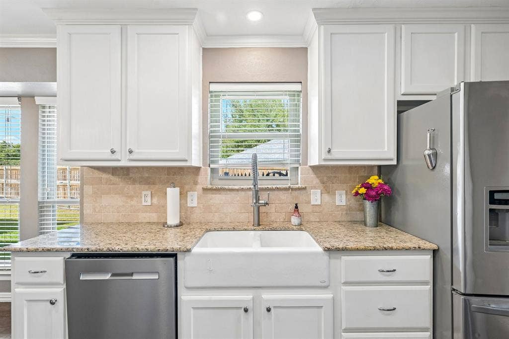 3441 Sheffield Circle, Plano, TX 75075 White shaker-style cabinetry with crown molding, light-toned granite countertops, a farmhouse-style sink, and a tiled backsplash