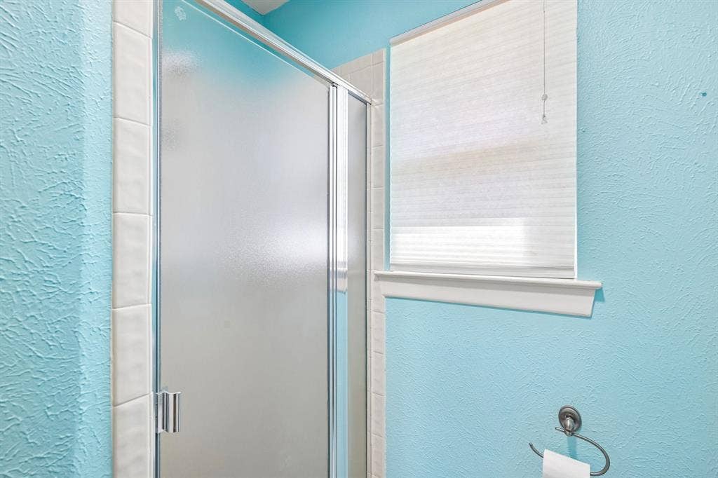 3441 Sheffield Circle, Plano, TX 75075 Frosted glass shower enclosure with chrome hardware, white tile surround, and textured blue walls