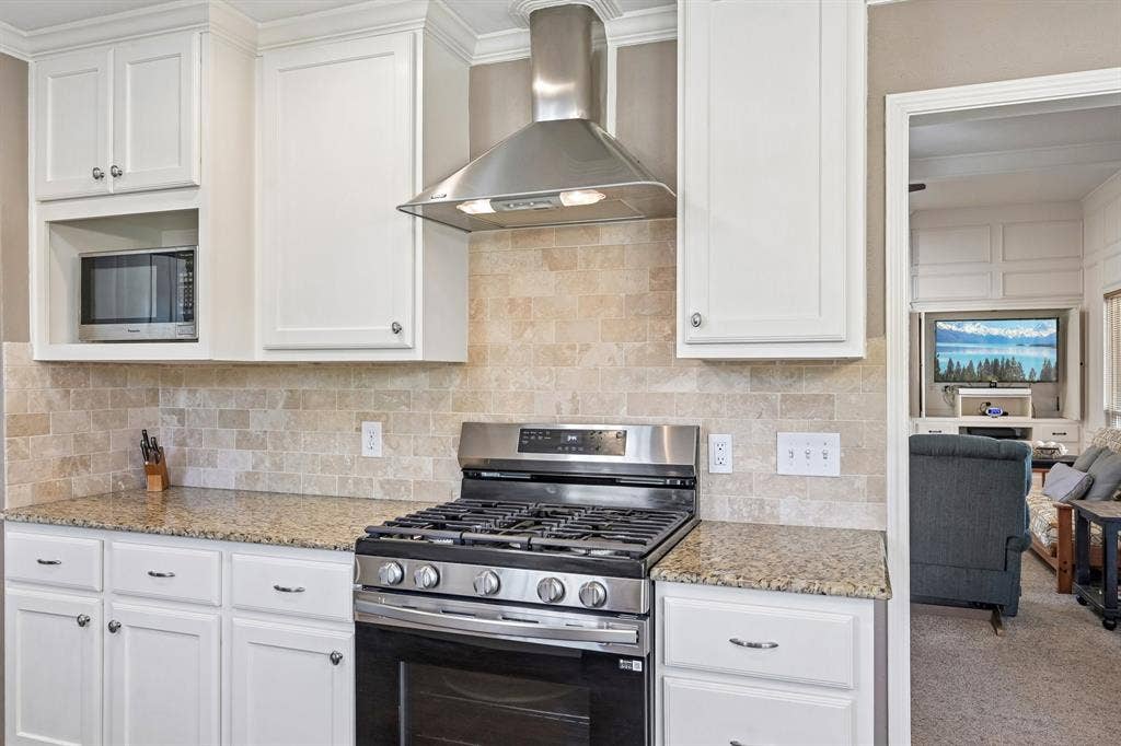 3441 Sheffield Circle, Plano, TX 75075 White cabinetry with crown molding, stainless steel range with overhead hood, integrated microwave, granite-finish countertops, and natural stone tile backsplash