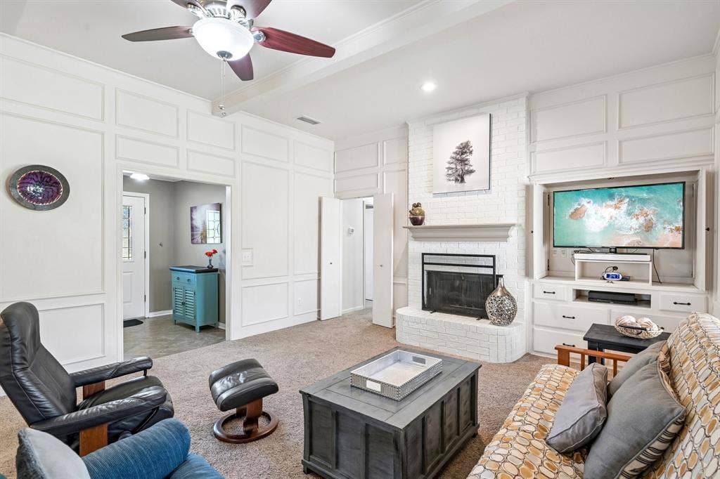 3441 Sheffield Circle, Plano, TX 75075 White paneled walls, ceiling fan with light fixture, brick fireplace with mantel, built-in entertainment center, and carpeted flooring