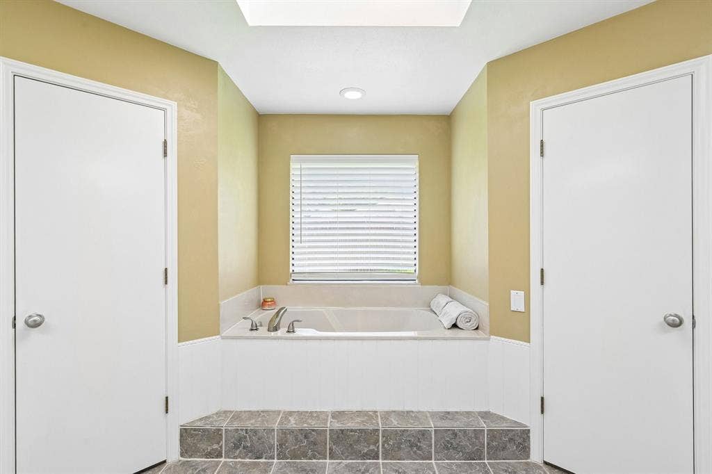 3441 Sheffield Circle, Plano, TX 75075 Recessed tub with tile surround, raised tile flooring, and overhead skylight