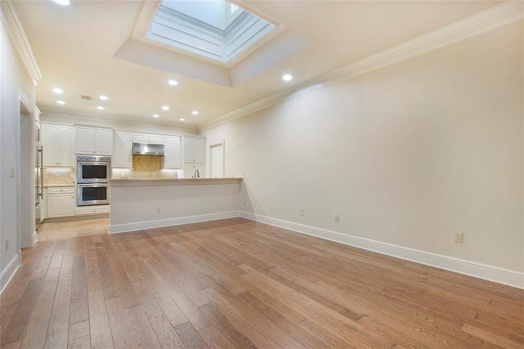 6425 Bandera Avenue, #2E, Dallas, TX 75225 Unfurnished living room with light hardwood / wood-style flooring, a tray ceiling, ornamental molding, and a skylight