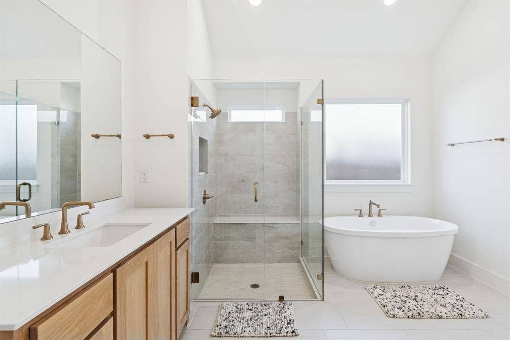 1117 Bradford Street, Celina, TX 75009 Spacious bathroom featuring a glass-enclosed shower with tiled bench, a freestanding soaking tub, and a double vanity with wood-finish cabinetry and solid surface countertop