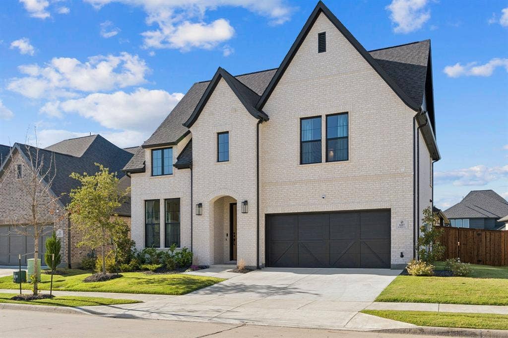 1117 Bradford Street, Celina, TX 75009 Two-story home featuring a light-colored brick exterior, dark-trimmed windows, a dark shingled roof, an arched entryway, and a dark-paneled garage door