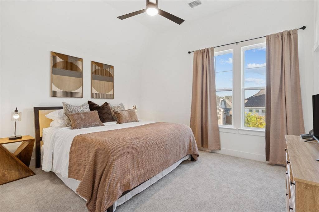1117 Bradford Street, Celina, TX 75009 Vaulted ceiling bedroom featuring a ceiling fan, plush gray carpeting, and two large windows with neutral curtains