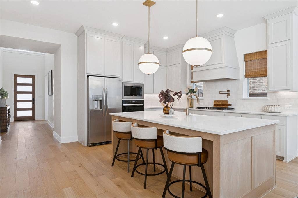 1117 Bradford Street, Celina, TX 75009 Gourmet kitchen featuring a substantial island with seating, pendant lighting, stainless steel appliances, a pot filler, and light wood-finish flooring