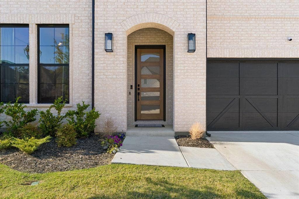 1117 Bradford Street, Celina, TX 75009 Contemporary brick exterior featuring a wood-finish entry door with glass panels, arched entryway, and modern black sconces