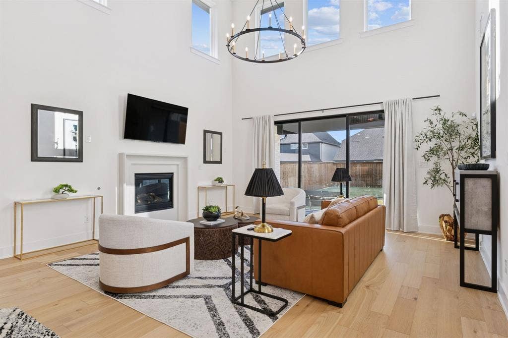 1117 Bradford Street, Celina, TX 75009 Light wood-finish flooring complements this living area featuring a tall ceiling, a sleek fireplace, and a large sliding glass door