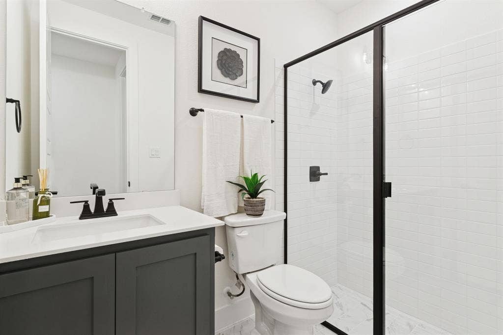 1117 Bradford Street, Celina, TX 75009 Bathroom featuring a dark gray vanity with white countertop, black fixtures, framed mirror, and a glass-enclosed shower with subway tile surround