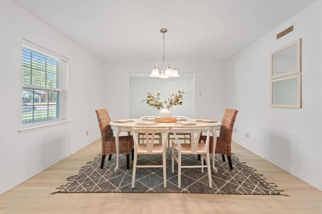 Bright, open space featuring new light wood-finish LVP flooring, a multi-bulb tiered chandelier, and a large window with horizontal blinds, ready to host family and friends for the holidays, bonus office space beyond dining area