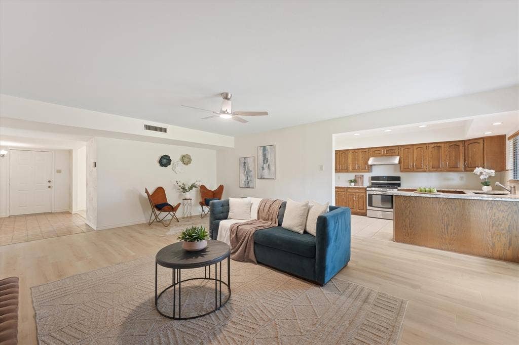 Open-concept living space featuring wood-finish flooring, ceiling fan with integrated lighting, kitchen with wood cabinetry, and a peninsula countertop