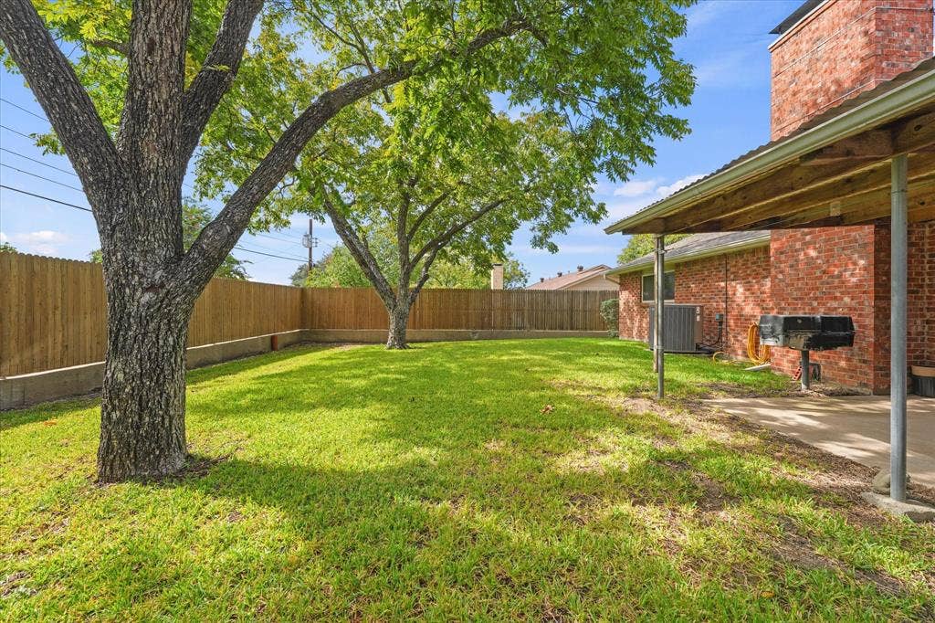 Private backyard featuring mature trees, a covered patio with a red brick exterior, and wood-style privacy fencing