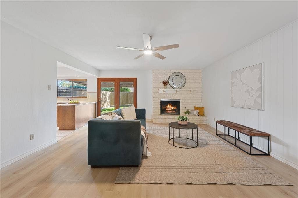 Living area featuring fresh interior paint, new light-toned LVP flooring, a brick gas fireplace, a built-in hearth, and new brushed nickel LED ceiling fan, natural light coming from covered patio