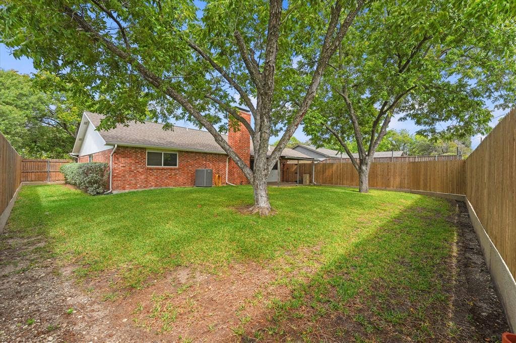 Expansive backyard featuring a brick exterior, mature trees, wood privacy fencing, and a red brick chimney