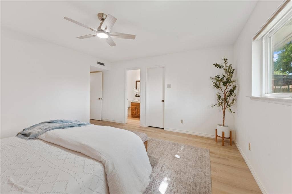 Neutral interior featuring light-tone wood-finish LVP flooring, white walls, a flush-mount ceiling fan with integrated lighting, and a double-pane window with influx of natural light
