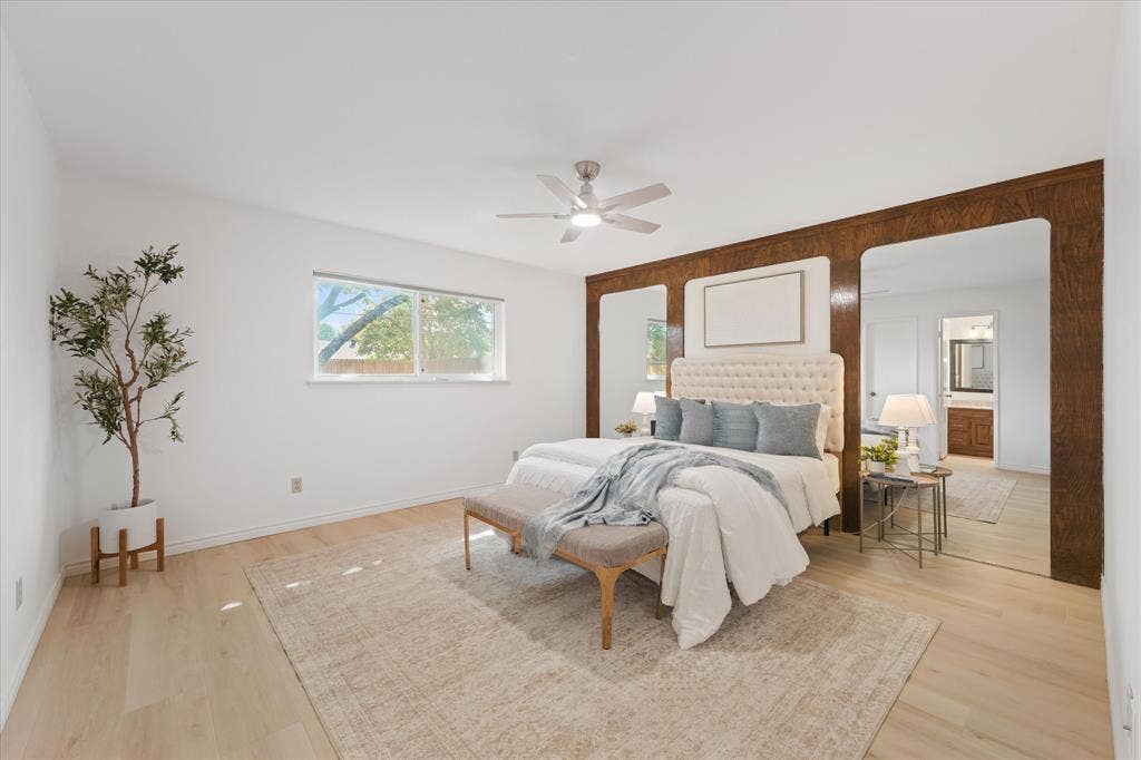 Large primary bedroom with wood-finish LVP flooring, custom wood-paneled accent wall with integrated mirrors, and new LED ceiling fan with 3 light tone options.