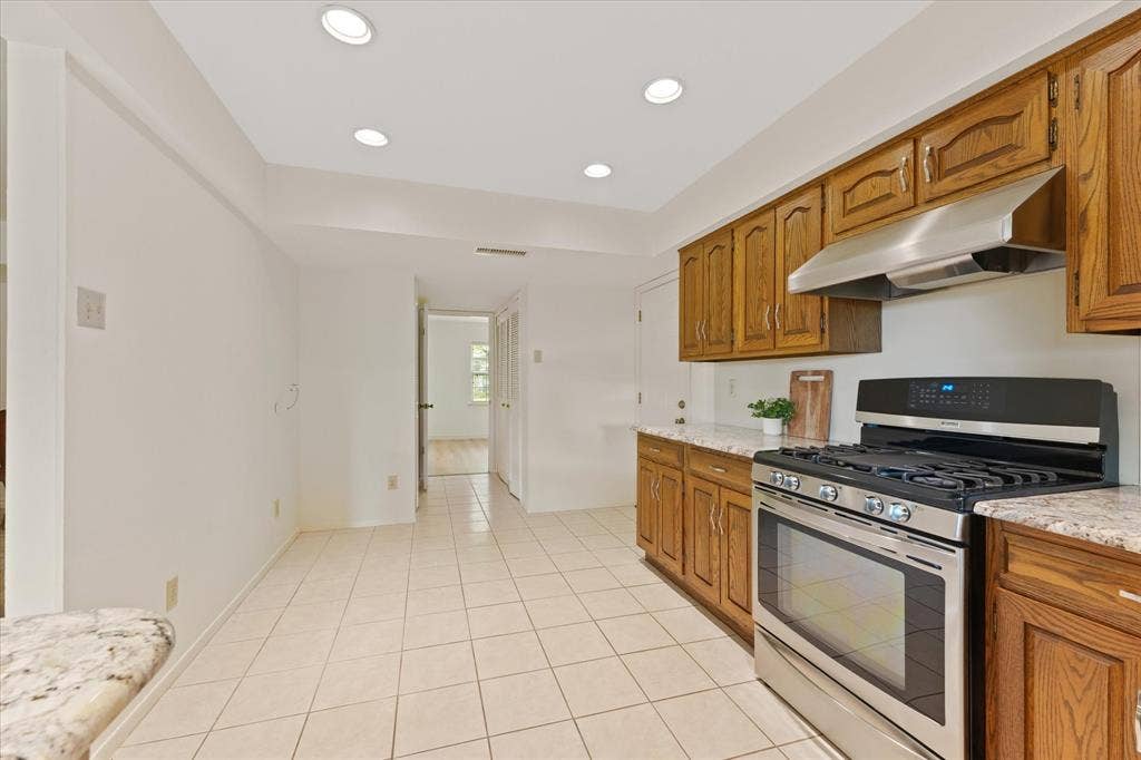 Eat in Kitchen featuring stained-wood cabinetry, stone-patterned countertops, stainless steel gas range, stainless steel range hood, and tile flooring