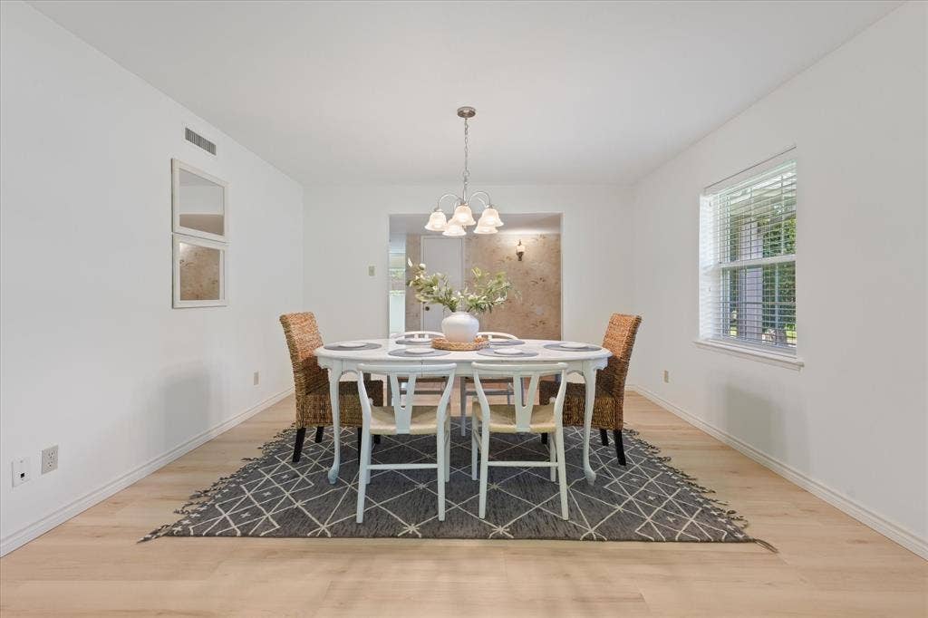 Dining space featuring light-toned wood-finish LVP flooring, a multi-bulb chandelier with frosted glass shades, and a double-pane window