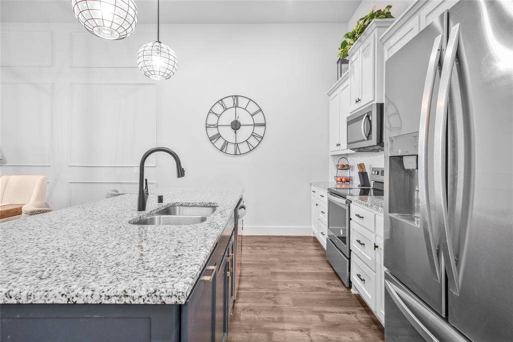 2644 Chardonnay Court, Grand Prairie, TX 75054 Kitchen featuring stainless steel appliances, granite countertops, wood-finish flooring, white upper cabinetry, and a central island with a sink and matte black faucet
