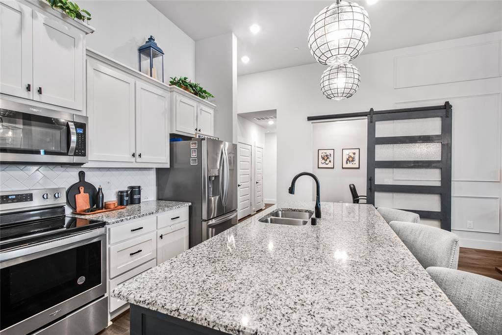 2644 Chardonnay Court, Grand Prairie, TX 75054 Kitchen featuring stainless steel appliances, white cabinetry, a tile backsplash, a large island with a double basin sink, and pendant lighting
