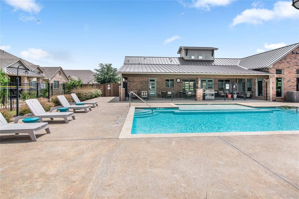 2644 Chardonnay Court, Grand Prairie, TX 75054 Resort-style resort pool with crystal-clear waters and sun loungers, anchored by a modern clubhouse featuring metal roofing, brick construction, and expansive glass doors