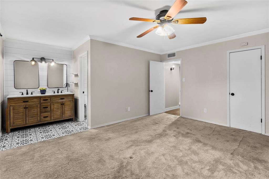 Spacious room featuring neutral carpeting, a ceiling fan, and crown molding